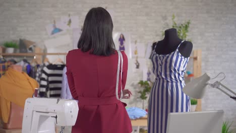 young female fashion designer sits with her back to the camera in a modern studio and makes sketches