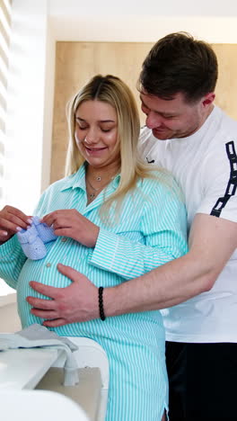 happy expecting couple stand in hospital ward hugging. woman holds the tiny socks for baby and man strokes her belly. vertical video