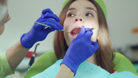 female dentist examining patient teeth with dental tools