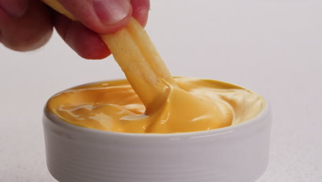 hand dipping french fries in cheese sauce