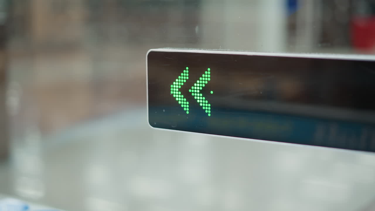 close up of green arrow display mounted at entrance of moving walkway in modern mall corridor with shadows of passing shoppers on glossy tiled floor under bright overhead lights indicating direction