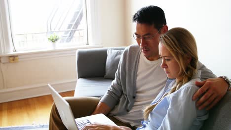 pareja usando una computadora portátil mientras se relaja en el sofá