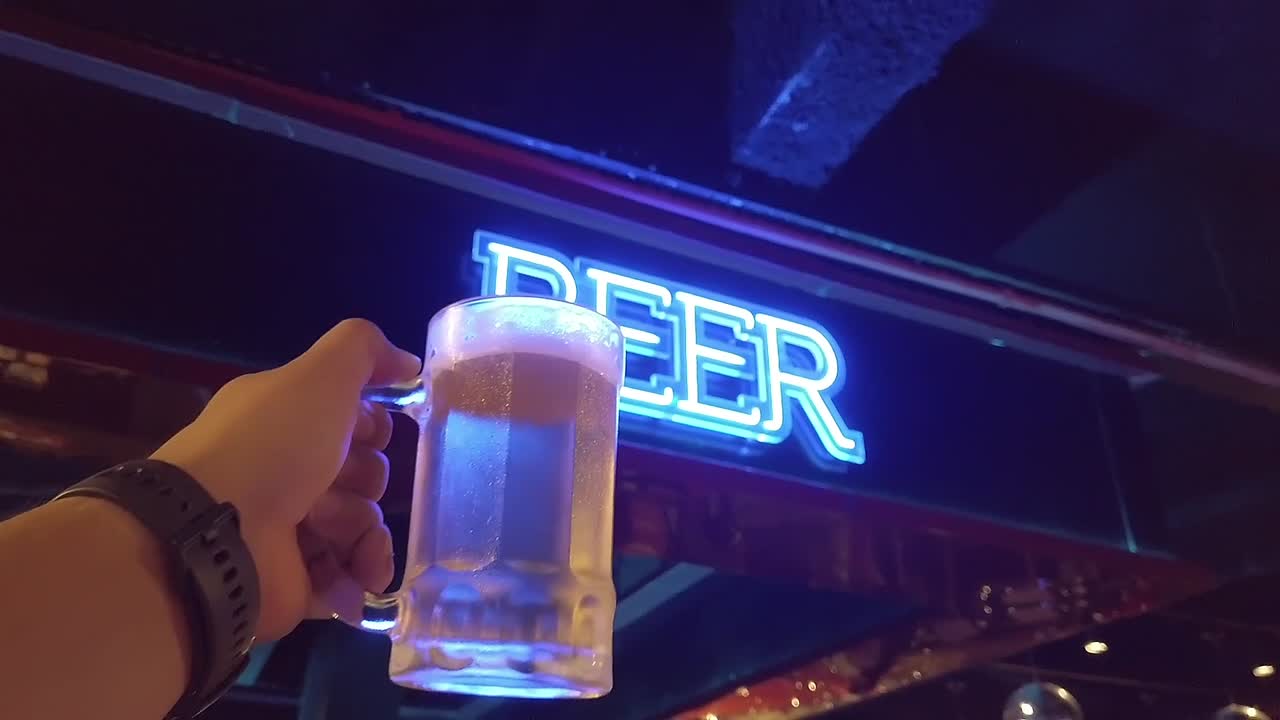 Man holding beer glass in hand against glowing neon beer signboard at a bar in Balneario Camboriu, Santa Catarina, Brazil