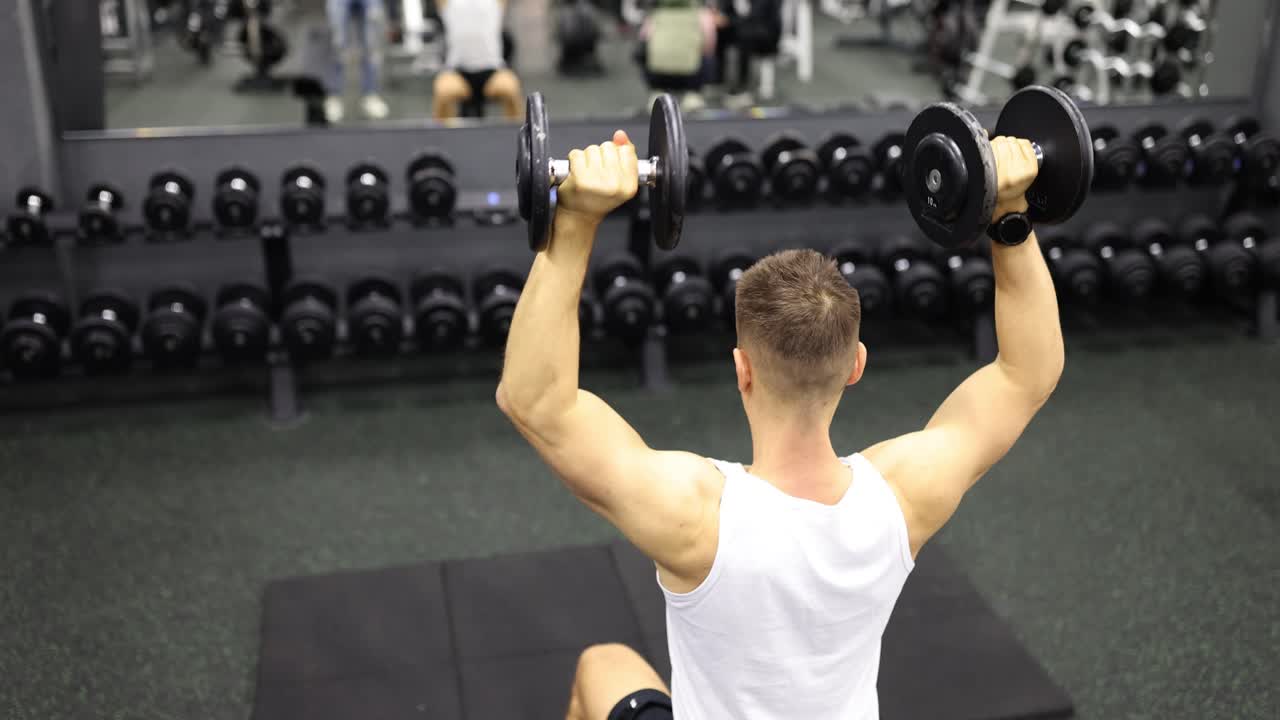 Man tilt zware dumbbells op terwijl hij in de sportschool zit
