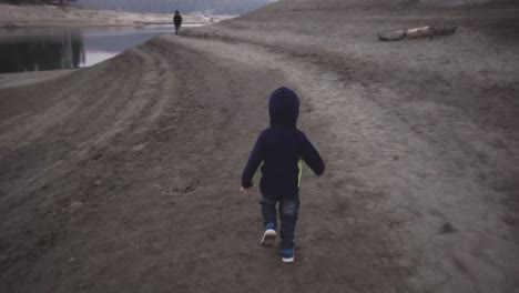 young boy in a hoodie runs alongs the beach at dusk, at shaver lake, california