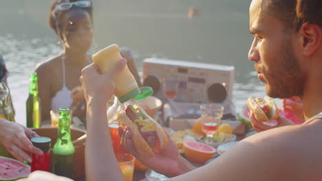 young man eating hot dog at lake party with friends