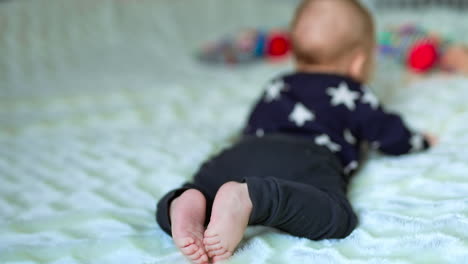 tiny baby lies on his belly and looks at the toy in front of him. little bare baby feet close up. white blurred backdrop.