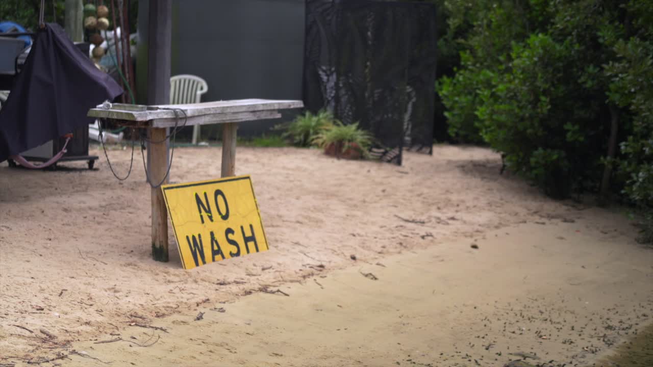 Handaufnahme eines gelben „No Wash“-Schildes an einem sandigen Flussufer am Hawkesbury River nahe Spencer, NSW.