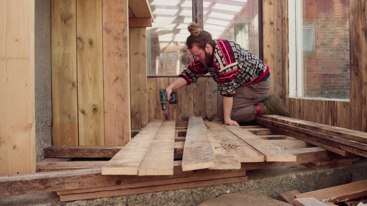 hombre usando herramienta de perforación eléctrica en la construcción de piso de madera para el invernadero - de cerca