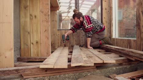 man using power drill tool in building wooden floor for the greenhouse - close up