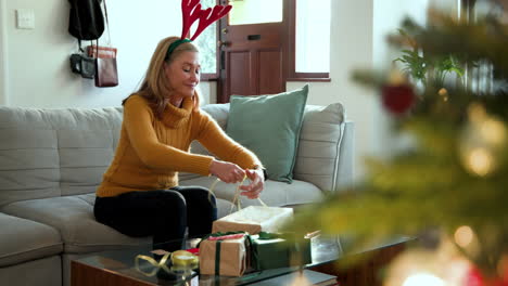 smiling woman wrapping christmas gifts at home, wearing festive reindeer headband