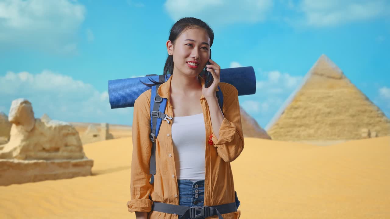 Asian Female Hiker With Mountaineering Backpack Smiling And Talking On Smartphone While Traveling In Pyramid Of Giza