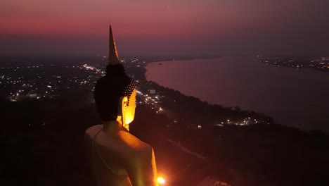 Golden-Buddha-overlooking-Mekong-river-vibrant-sunset,-Pakse,-Laos