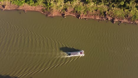 aerial tracking shot of tourist boat cruising on iguazu river during sunny day between argentina and brazil country