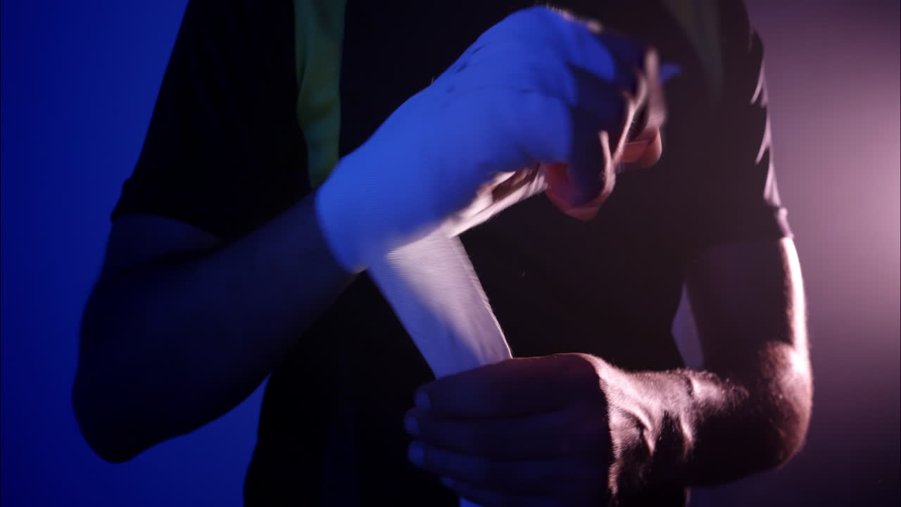 Male Boxer Wrapping Hands with White Hand Wraps in Dark Gym