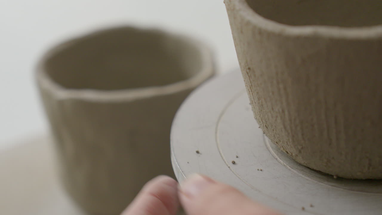 Fingers turn a wheel of a clay cup's form, close-up glimpse into an artisan's magical creation