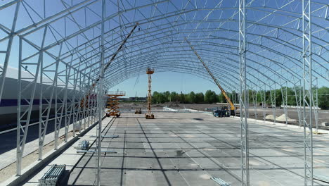 massive grain warehouse under construction with heavy cranes, aerial drone view