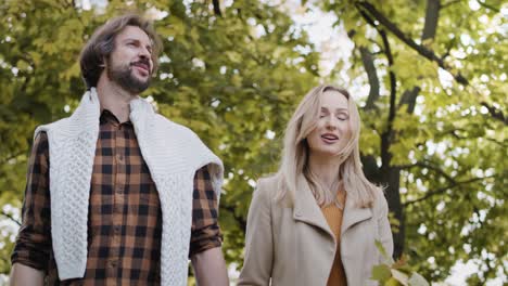 Low-angle-view-of-happy-couple-walking-in-autumn-forest