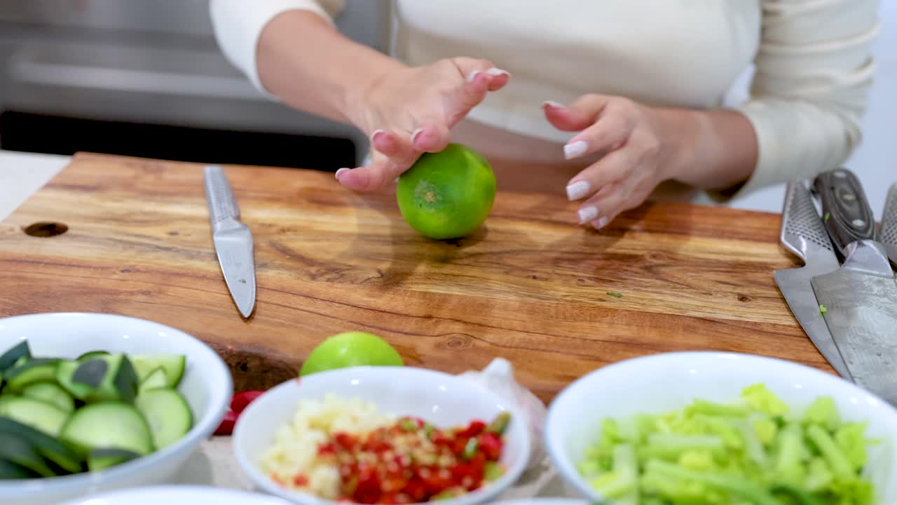 A person rolls a lime on a wooden cutting board in a bright kitchen setting
