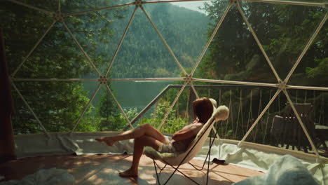 woman sits alone at contemporary room with stunning mountain view. brunette lady enjoys free time sitting in cozy armchair. concept of escaping from everyday life