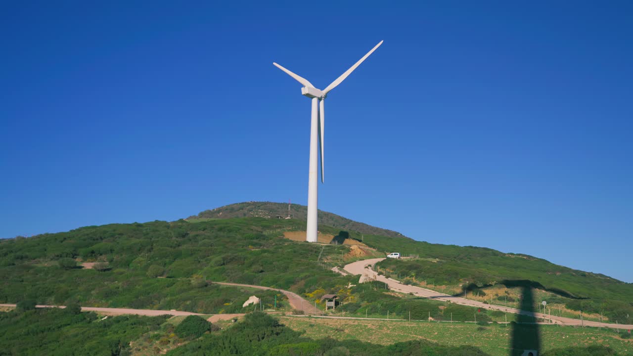 배경 에 은 파란 하늘 이 있는 언덕 꼭대기 에 있는 풍력 터빈