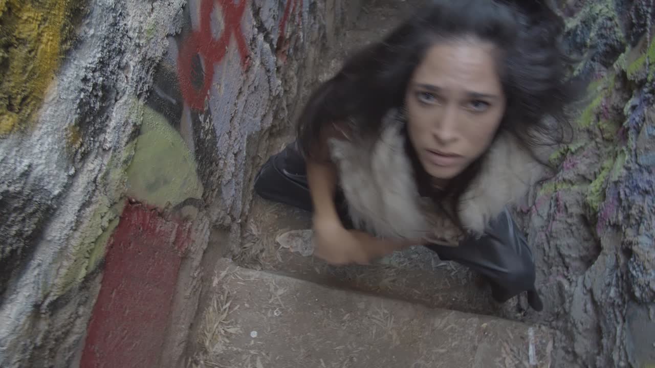High angle of an interpretive dancer looking at her hands and then intensely towards the camera in a colorful abandoned stairway