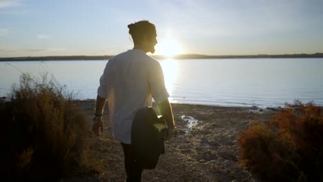 man walking with guitar on the beach at sunset