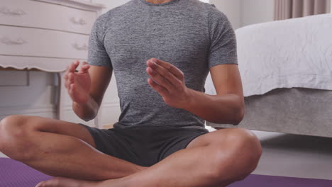 close up dolly shot of man sitting on yoga mat in bedroom at home joining hands together - shot in slow motion