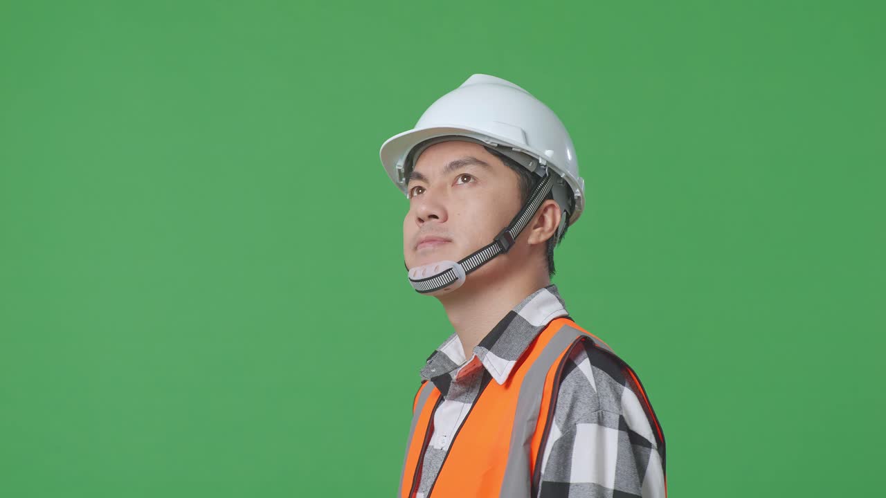 Close Up Side View Of Asian Male Engineer With Safety Helmet Looking Around While Standing In The Green Screen Background Studio