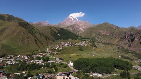 drone ascends above mountain village with mount kazbek in background