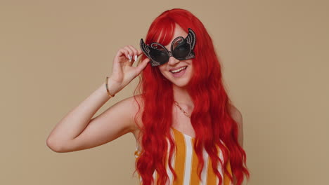 Seductive-cheerful-stylish-redhead-girl-in-tank-top-wearing-sunglasses,-charming-smile-on-beige-wall