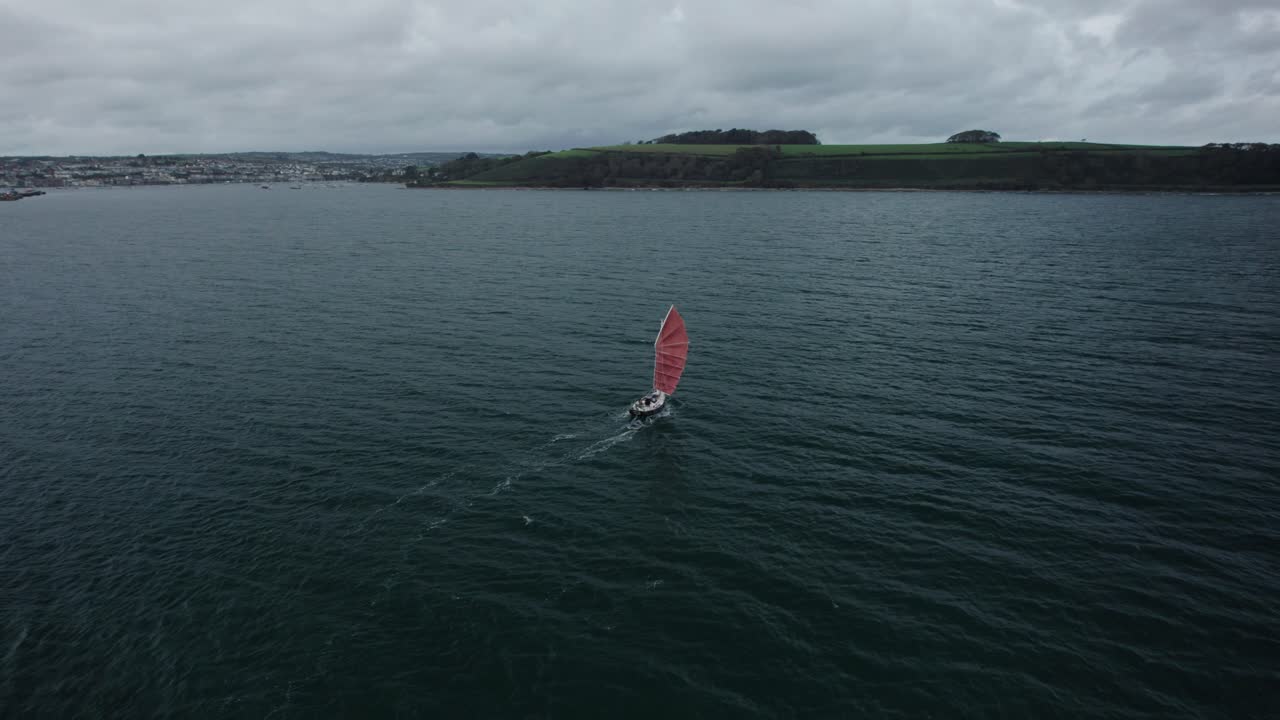 pequeño velero vintage con velas de borgoña, en un clima inglés sombrío