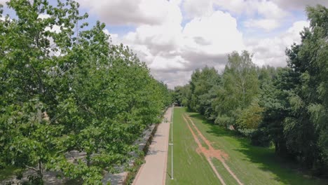 Un-Vuelo-Cerca-De-Los-árboles-Sobre-El-Carril-Bici,-Espacio-Verde-En-Un-Lugar-Seguro-Con-Linternas-Y-Una-Acera,-Un-Lugar-Para-Descansar-Fuera-De-La-Ciudad,-Tiro-Aéreo-En-4k