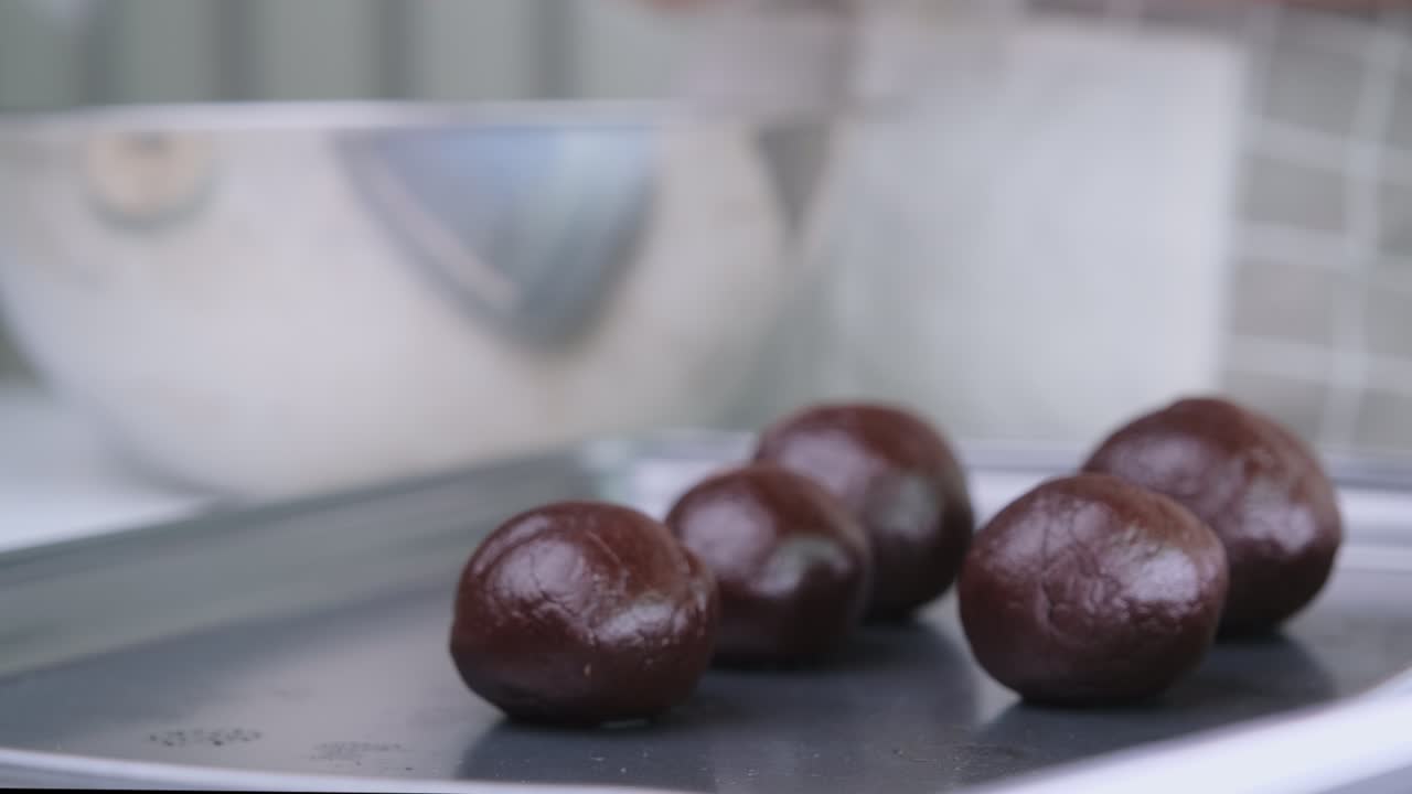 manos con guantes desechables están haciendo bolas de cacao caseras rellenas con cubos de chocolate oscuro y colocándolas en una bandeja.