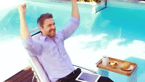 Handsome-man-using-tablet-on-deck-chair-and-cheering