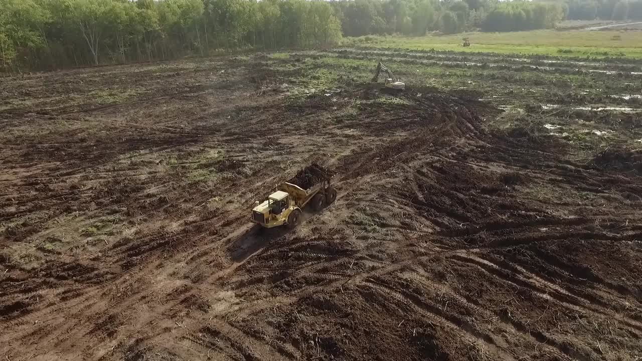 Large earth moving construction scraper twists and turns loaded with mud and earth as it works to reshape the land. Overhead aerial shot