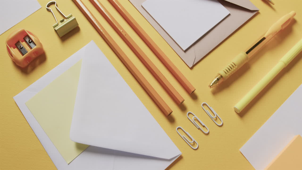 Close up of pens, pencils and stationery arranged on yellow background, in slow motion