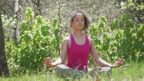 mujer biracial vestida con ropa deportiva y meditando en el bosque