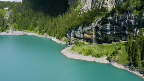 aerial of hikers walking underneath cliffs with a small waterfall running into a beautiful lake