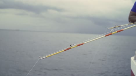 close up of two fishing rods bent off the side of a boat in the ocean, moving up and down in the morning, clouds