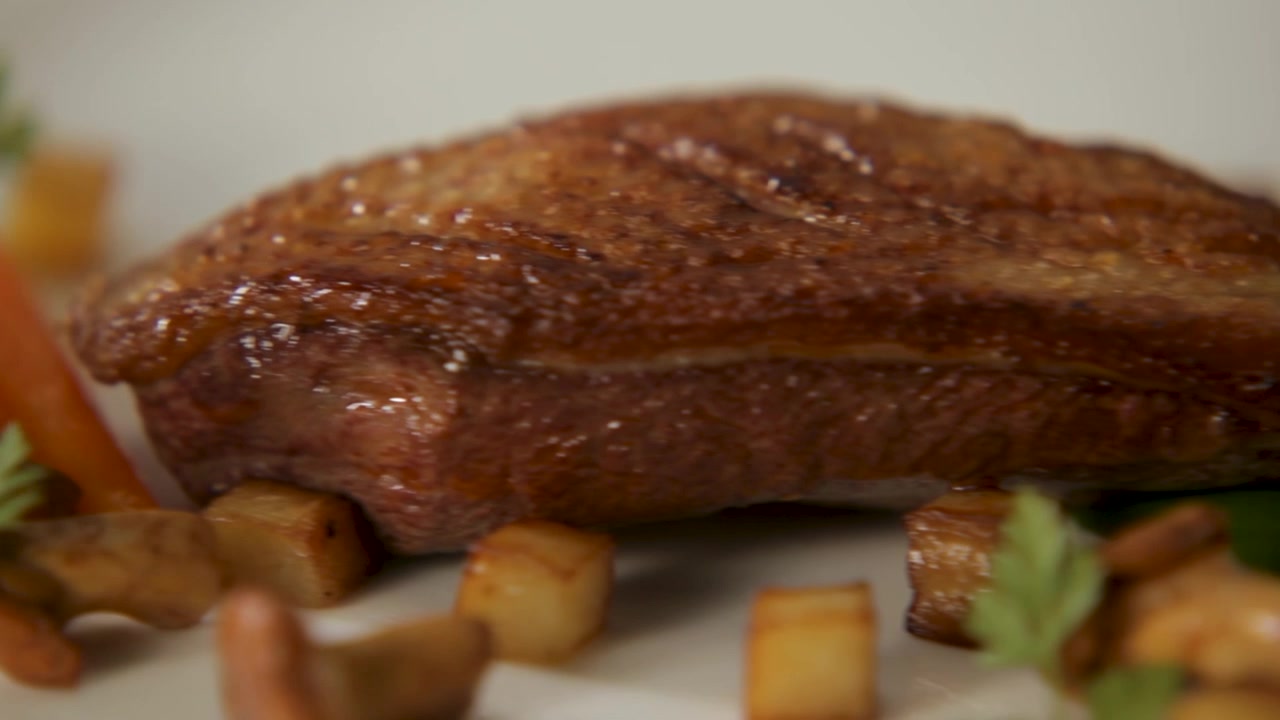Gourmet dish of seared meat with mushrooms, diced potatoes, and carrots on a white plate