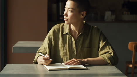 person writing and reflecting in a notebook at a cafe