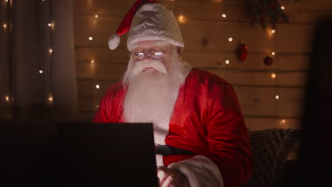 Fernarbeit-Des-Weihnachtsmanns.-Online-Shopping-Und-Bestellung-Der-Lieferung-Von-Geschenken.-Der-Weihnachtsmann-Arbeitet-Am-Heiligabend-Zu-Hause-Mit-Einem-Laptop.-Weihnachtsbeleuchtung-Und-Dekoration