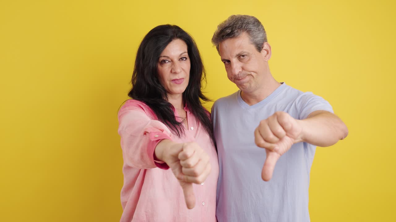 Couple giving thumbs down on yellow background