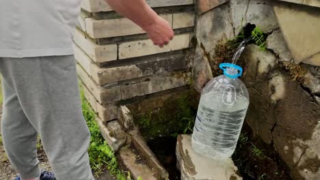 person filling a bottle with free natural spring mineral water from village well supply