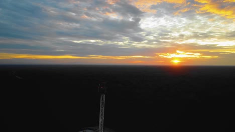 imágenes cinematográficas de drones de la estructura del equipo de la plataforma de perforación en tierra para la exploración y explotación de petróleo en medio de la jungla rodeada de palmeras durante la puesta de sol y el alto precio del petróleo