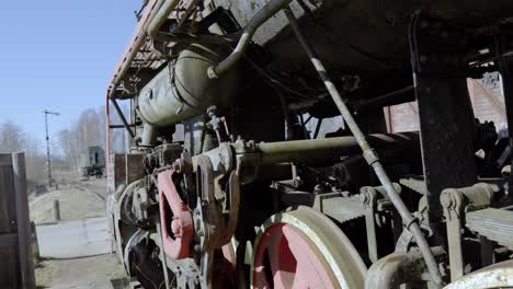 close-up of the trai wheels of a red locomotive parked on a railroad track in a rural area