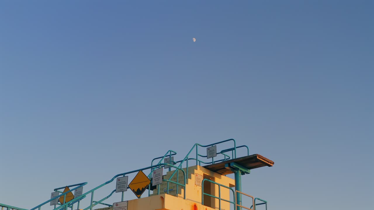 Aerial dolly shot of the outdoor diving board at sunset, with the moon and blue sky. Salthill, Galway