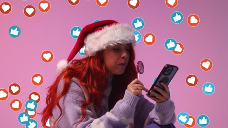 gen z mulher vestindo chapéu de papai noel comendo doce pirulito olhando para o telefone móvel com emojis de gráficos de movimento mostrando várias notificações de mídia social gostando e reagindo ao conteúdo on-line