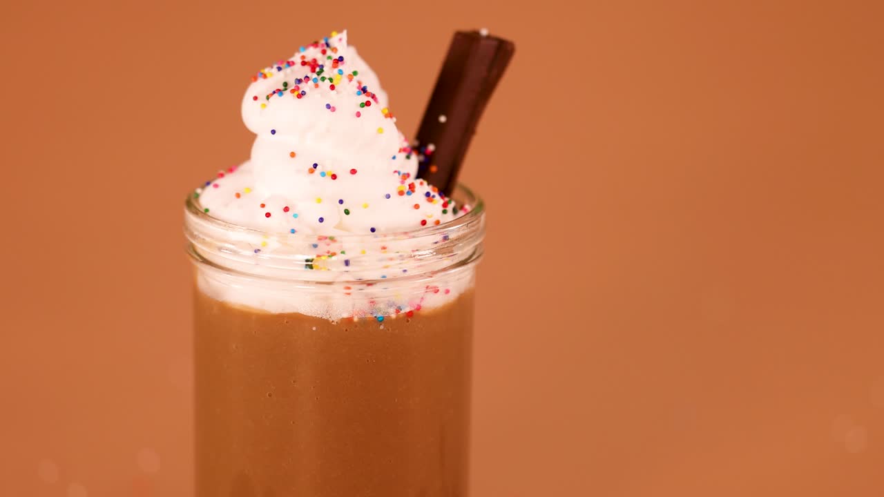 Chocolate milkshake with whipped cream, sprinkles, cookies, and chocolate bars, smooth camera downward movement